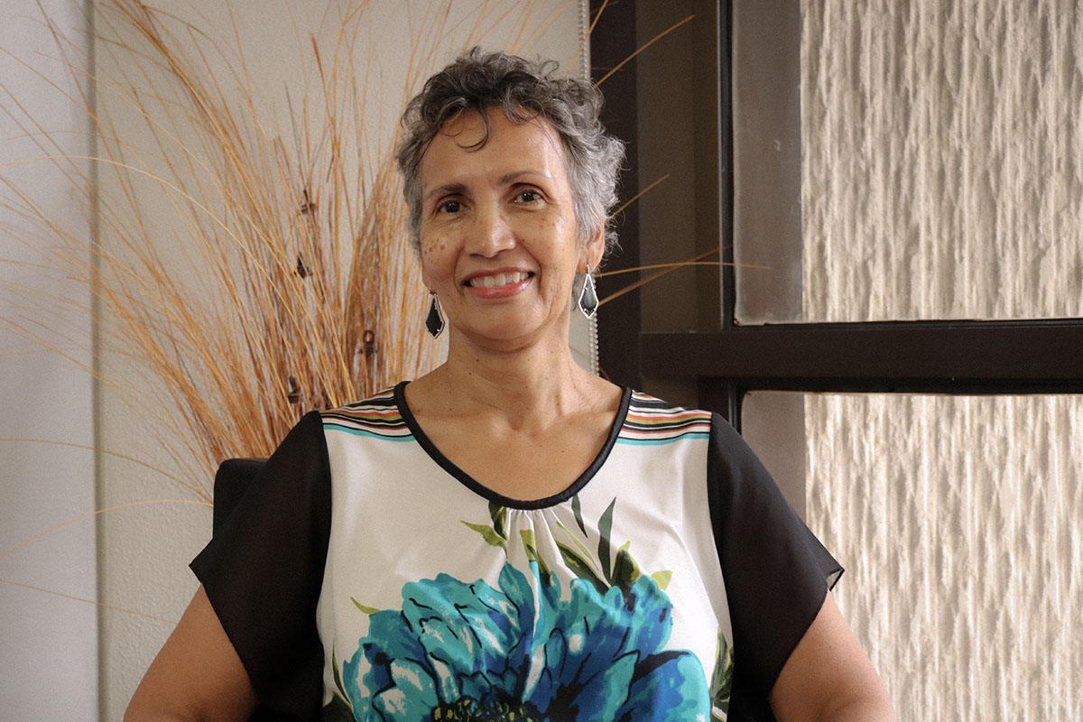 image of lorraine haricombe, smiling, sitting in front of a window in a colorful blouse