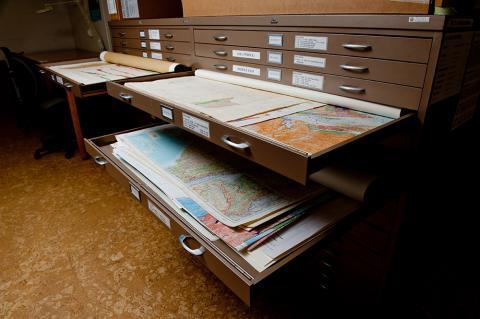 numerous steel flat files, drawers open, containing maps from around the world