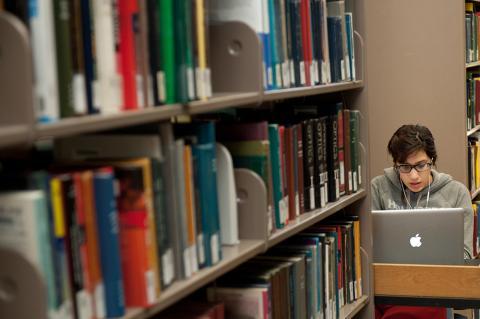 Student on a laptop adjacent to a shelf of books