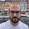 portrait of man in glasses with beard in front of european style canal with houses in the background