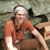 man in orange shirt and headband sitting in front of stones smiling