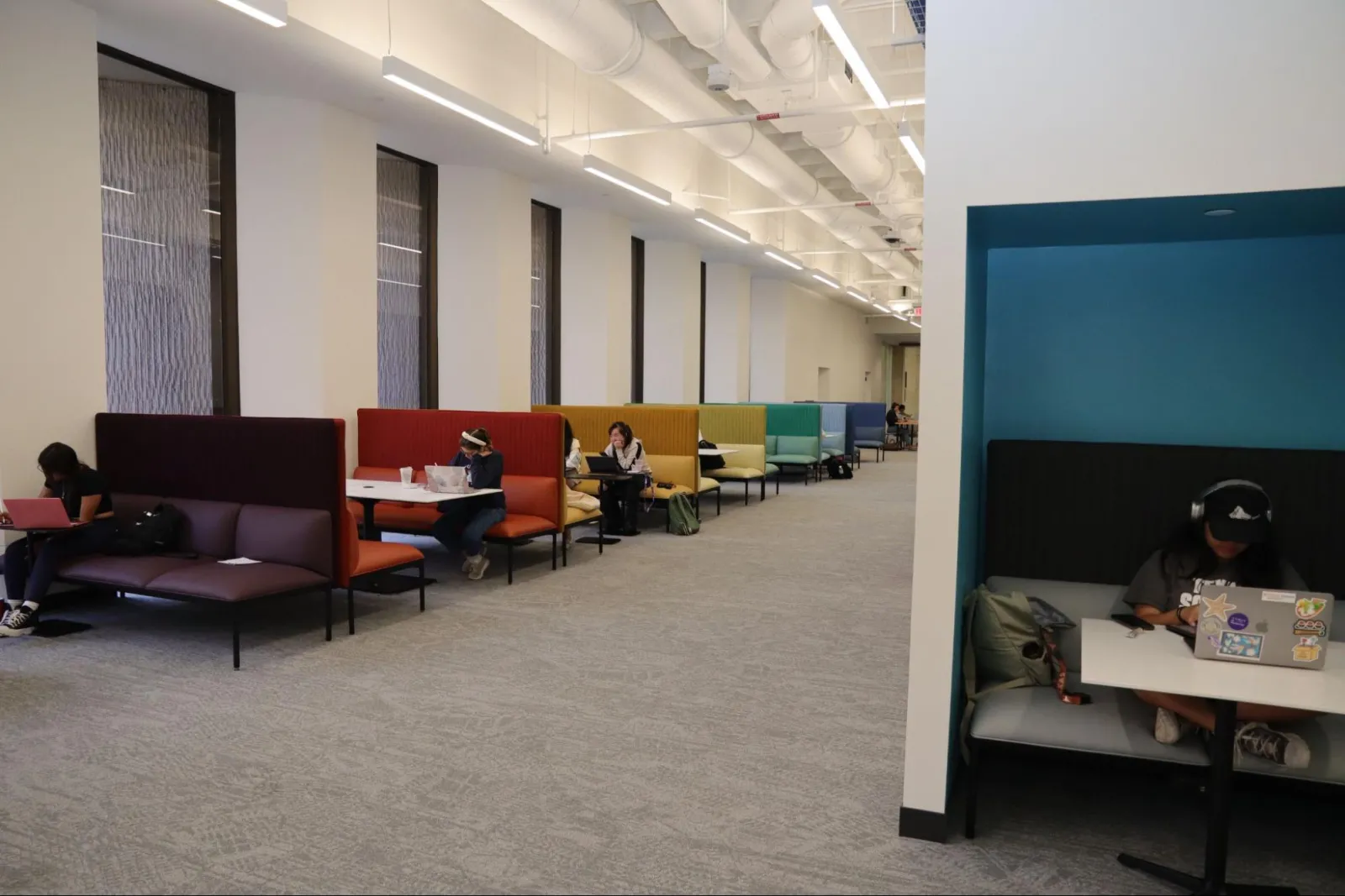 The open study space in the Scholars Lab features colorful couches near large windows. Additionally, there is a couch positioned on the right side of the colorful couches, adjacent to a wall. Individuals can be seen reading or using laptops.