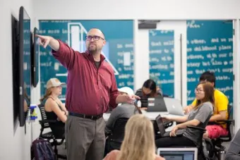 Person pointing, in an instructor fashion, to a monitor mounted on the wall